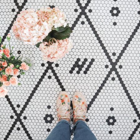 Aerial view of person wearing pink floral sneakers standing beside pink floral arrangement on patterned tiles