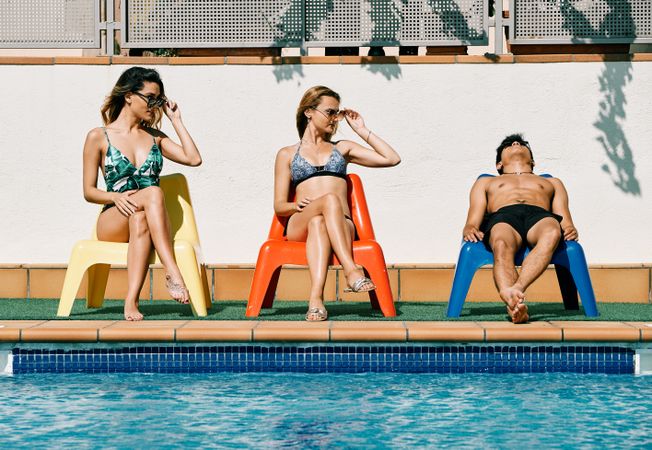 two young women looking at a handsome man by the pool