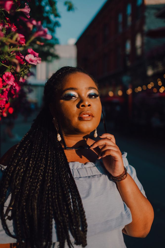 Joyful trendy Black woman standing beside blossomed tree