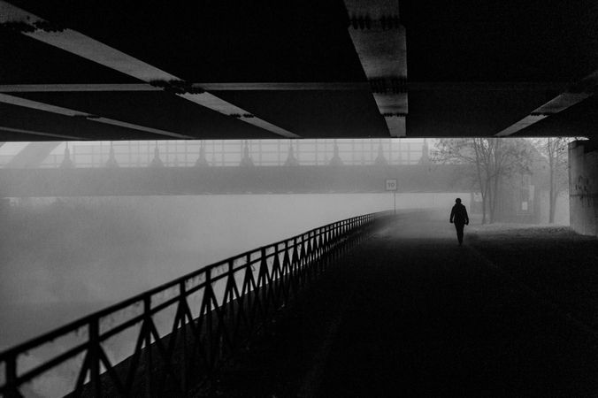Grayscale photo of silhouette of person walking on bridge