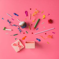 Gift box with colorful party items on pink background