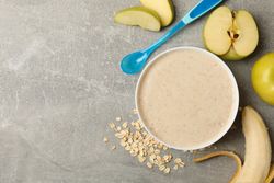 Bowl with porridge on gray background, top view. Baby food