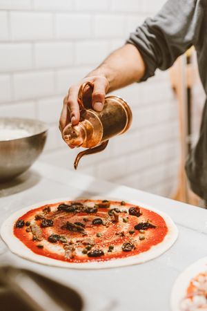 Cropped image of person adding olive oil on a pizza