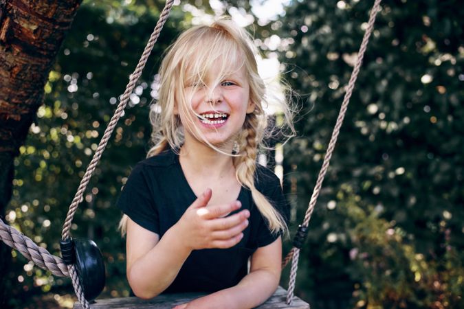 Smiling blonde girl with braided hair playing on outdoor swing