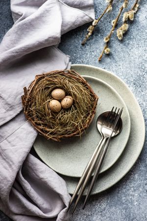 Top view of decorative eggs in delicate nest on ceramic grey plate on table
