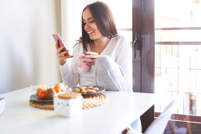 Smiling woman with smartphone eating at table at home