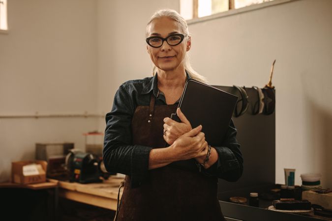 Portrait of mature female jeweler in her workshop with a book