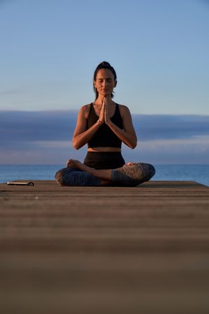 Peaceful Hispanic woman meditating on boardwalk near sea