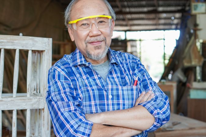 Portrait of mature Asian male carpenter with arms crossed at carpentry workshop