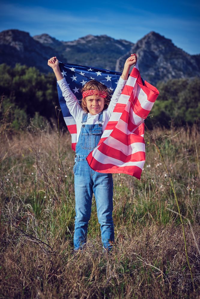 Proud preteen boy raising hands with American national flag
