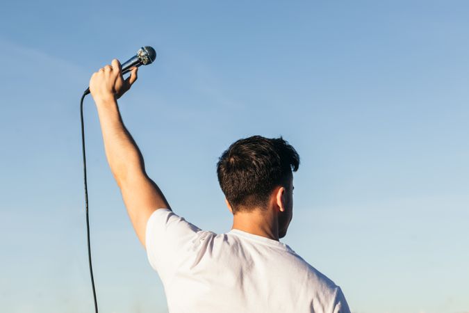 back view of a man with arm raised holding a microphone