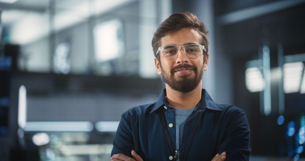 Indian Wearing Glasses and a Dark Blue Shirt Smiling and Looking at Camera.