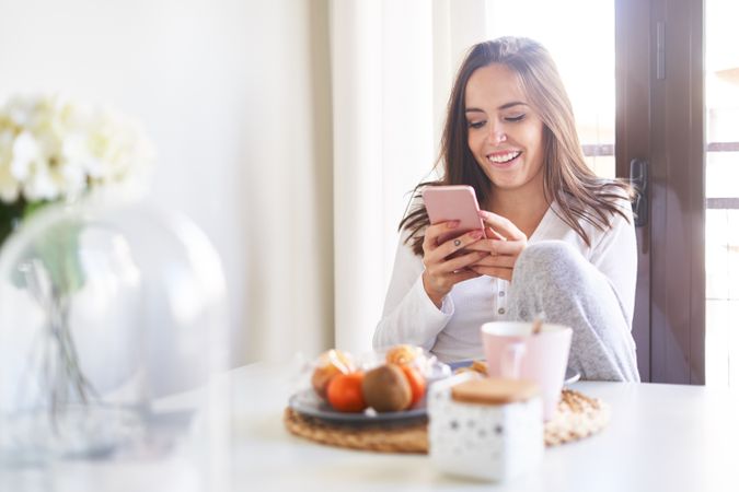 Smiling woman with smartphone eating at table at home