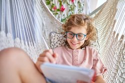 Happy boy taking notes in notepad in hammock