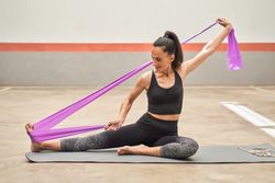 Smiling female athlete stretching leg on mat with elastic band