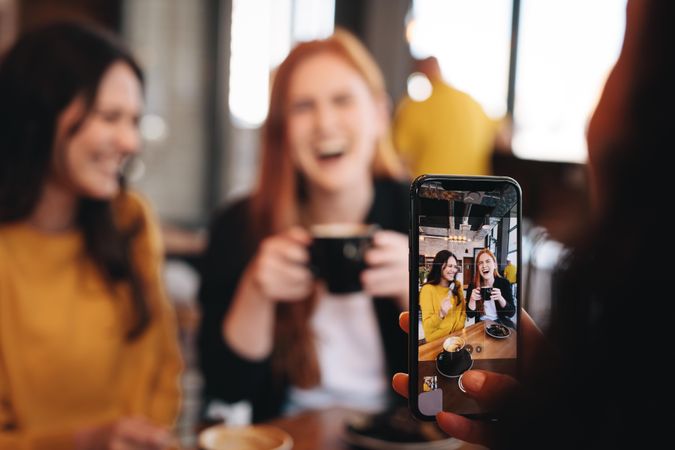 Woman taking photo of her friends with her smart phone at a coffee shop
