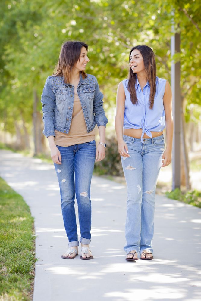 Young Adult Twin Sisters Walking Together On Sunny Day