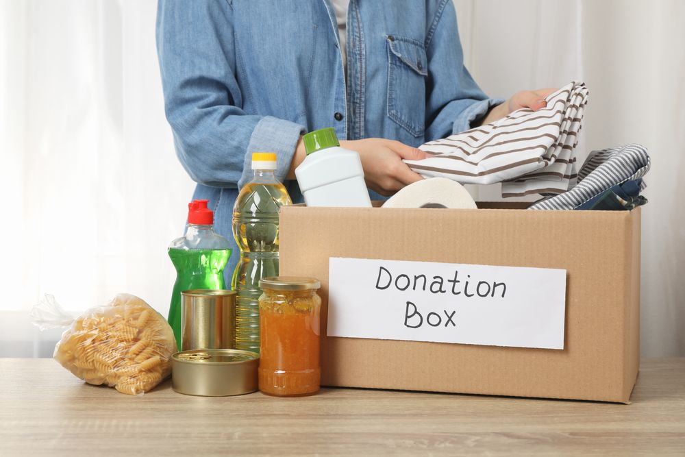 Woman puts clothes in donation box on wooden table