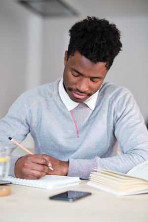 Black student with notebook and book studying in house