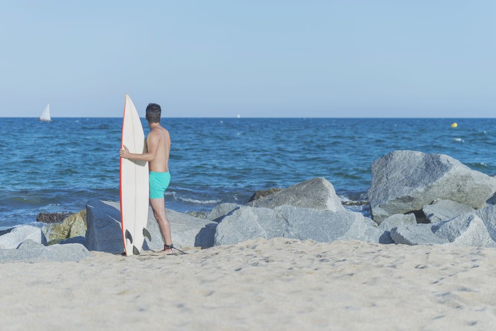Back of male surfer standing on rock near ocean with board