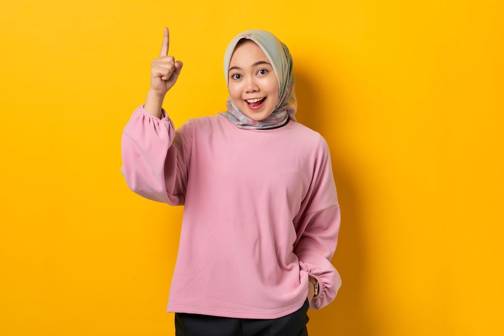 Smiling Muslim woman smiling and pointing upwards with good idea