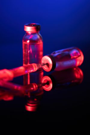 Syringe inserted into vial under neon lighting