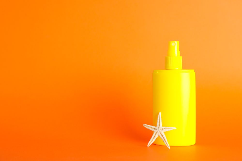 Sunscreen spray with starfish on color background, space for text