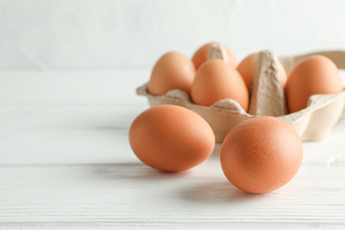 Brown chicken eggs in carton box on light background, space for text and closeup