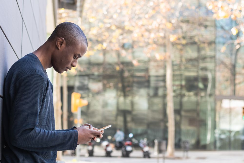 Serious Black man using smartphone against gray wall