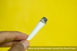 Side view of hand holding lit hand rolled cigarette on yellow background 5qkD7q