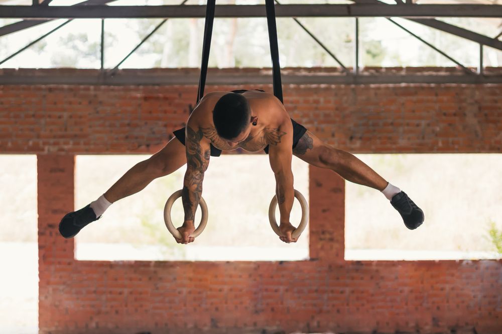 man athlete training in gymnastic rings doing a straddle planche