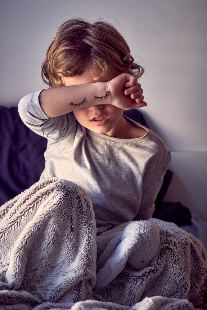 Tired boy covering eyes with hand with painted eyelashes