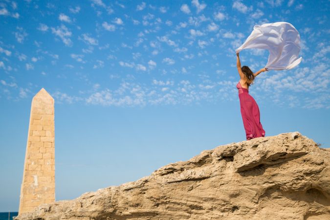 Woman in dress with scarf in upped hands near stone monument