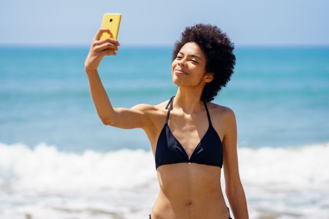 Smiling woman in biking standing near the ocean taking a selfie