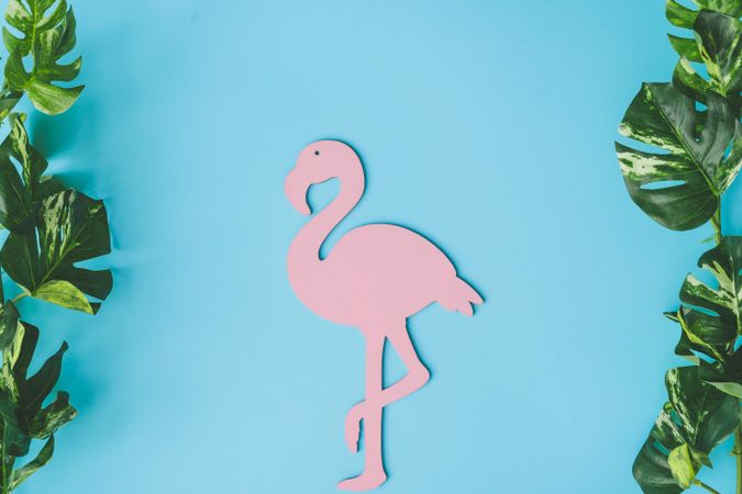 Pink flamingo shape with green tropical leaves on bright blue background