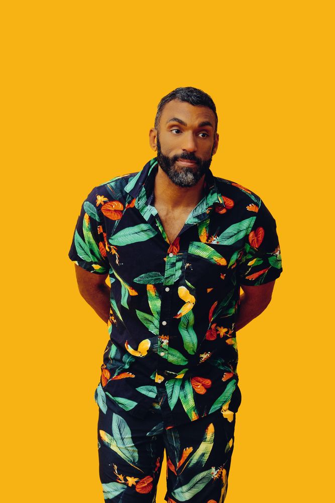 Black male in bold patterned shirt standing in yellow room