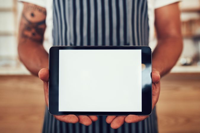 Close up portrait of a man wearing an apron holding a digital tablet with a blank white screen