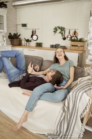 Chilling couple spending time together on sofa browsing smartphone
