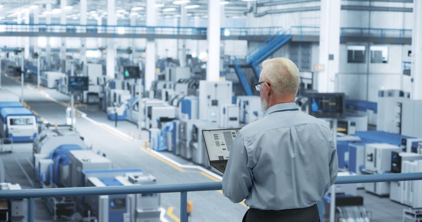 Portrait of an Adult Engineer Standing on a Platform, Using Laptop Computer at an Electronics Factory. Technician Making Technical Upgrades Online Over an Internet Software