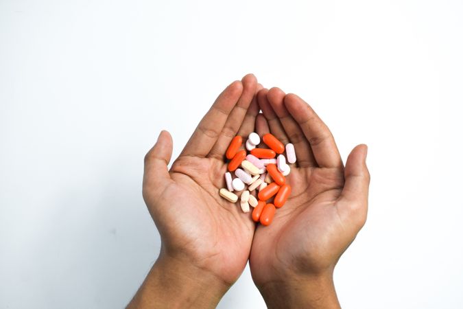 Hands holding variety of colorful medication and vitamins with plain background