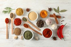 Top view of four wooden scoop full of peppercorn with bowls of spice