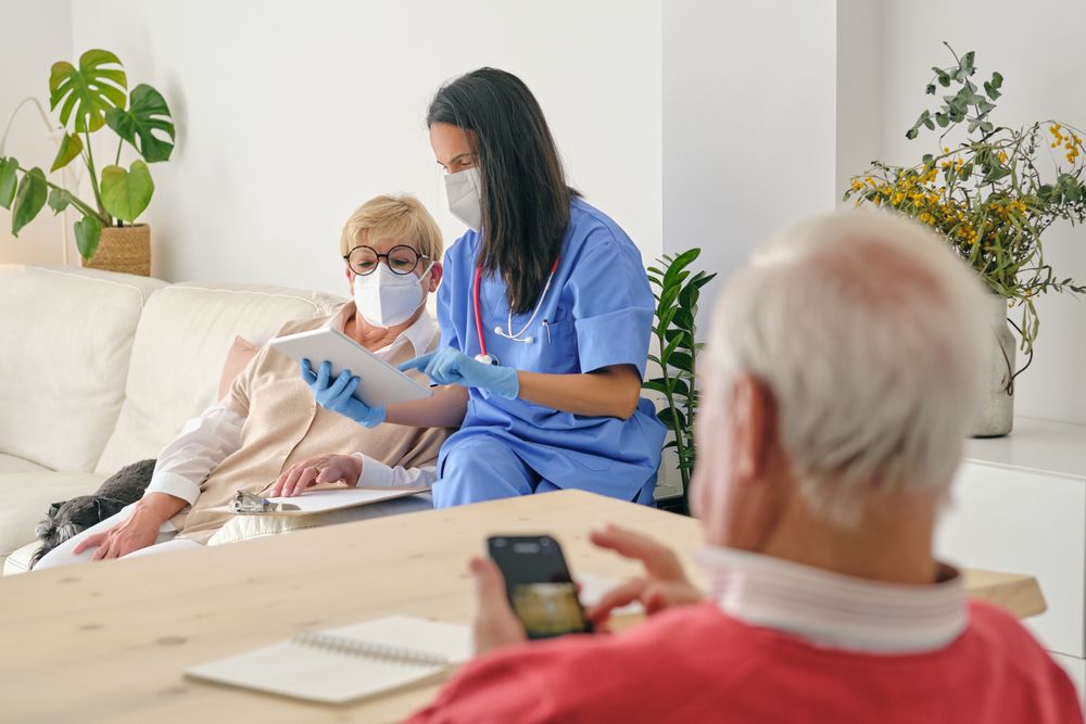 Doctor sharing tablet with mature patient against man at home