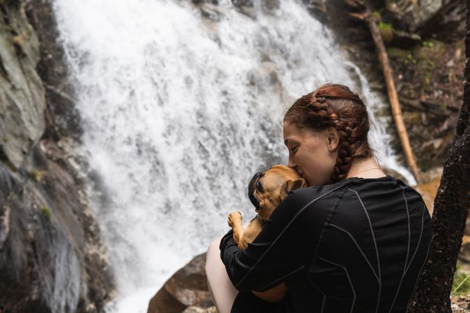 Cheerful traveling woman with dog near waterfall in forest