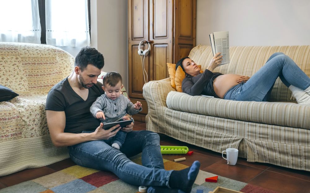 Father looking tablet with little son while the pregnant mother reads a magazine