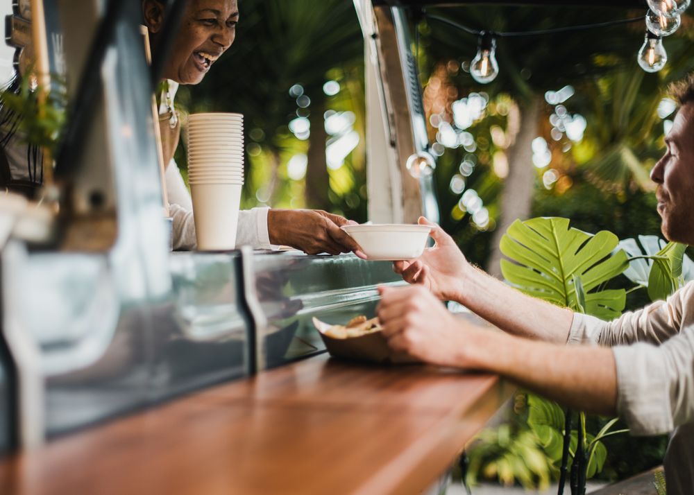 Woman serving food to customer inside food truck - Focus on hands holding food plate
