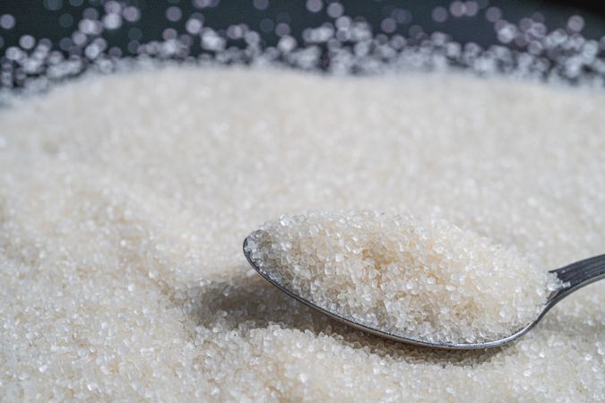 Granulated sugar spread on a surface with a spoonful resting on top