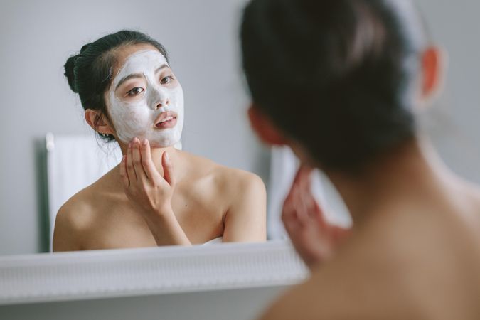 Woman with facial mask in front of bathroom mirror