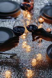 Two hands holding wine glasses cheers over a set dinner table