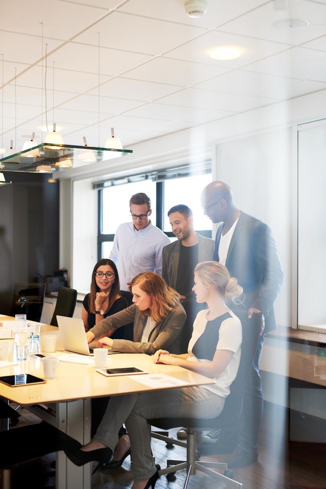 Multi-ethnic group of colleagues surround a woman on her laptop