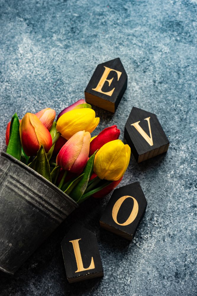 Valentine's day card concept with the word "love" and metal vase of tulips on grey counter